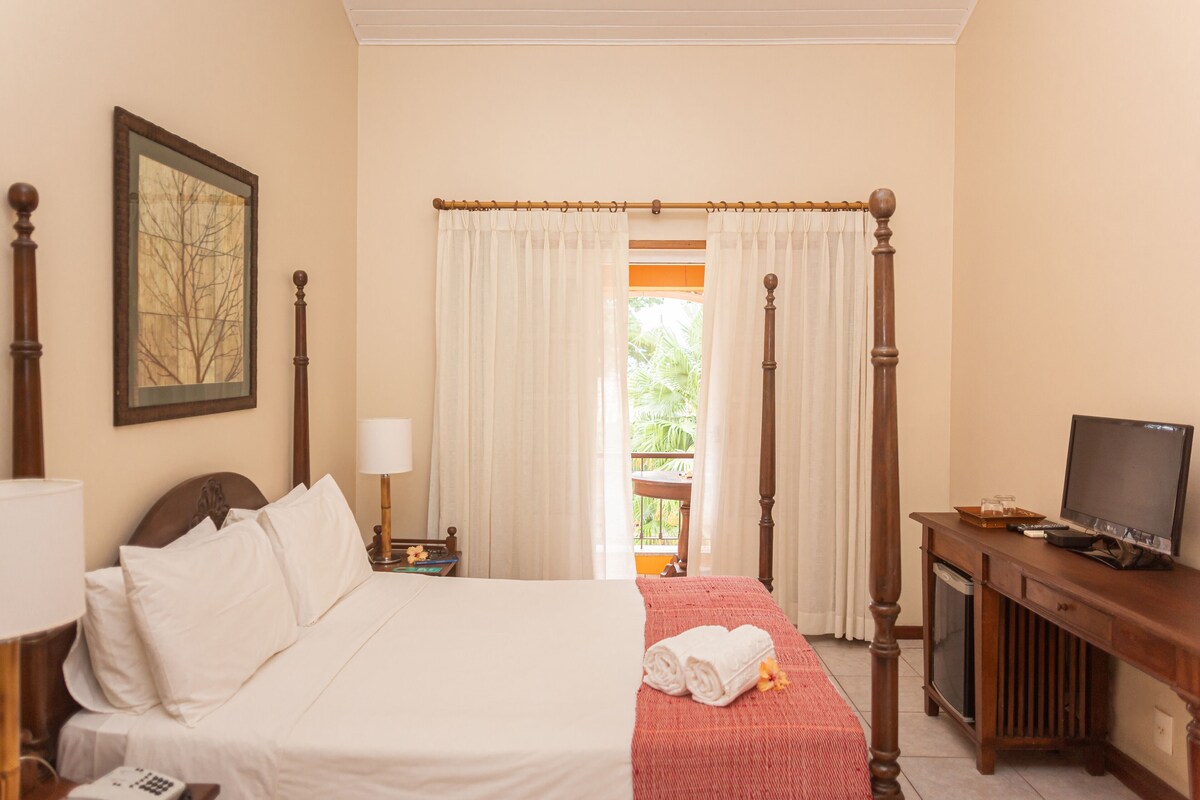A hotel room with a bed, a television, a desk with a tray, and a window with curtains.