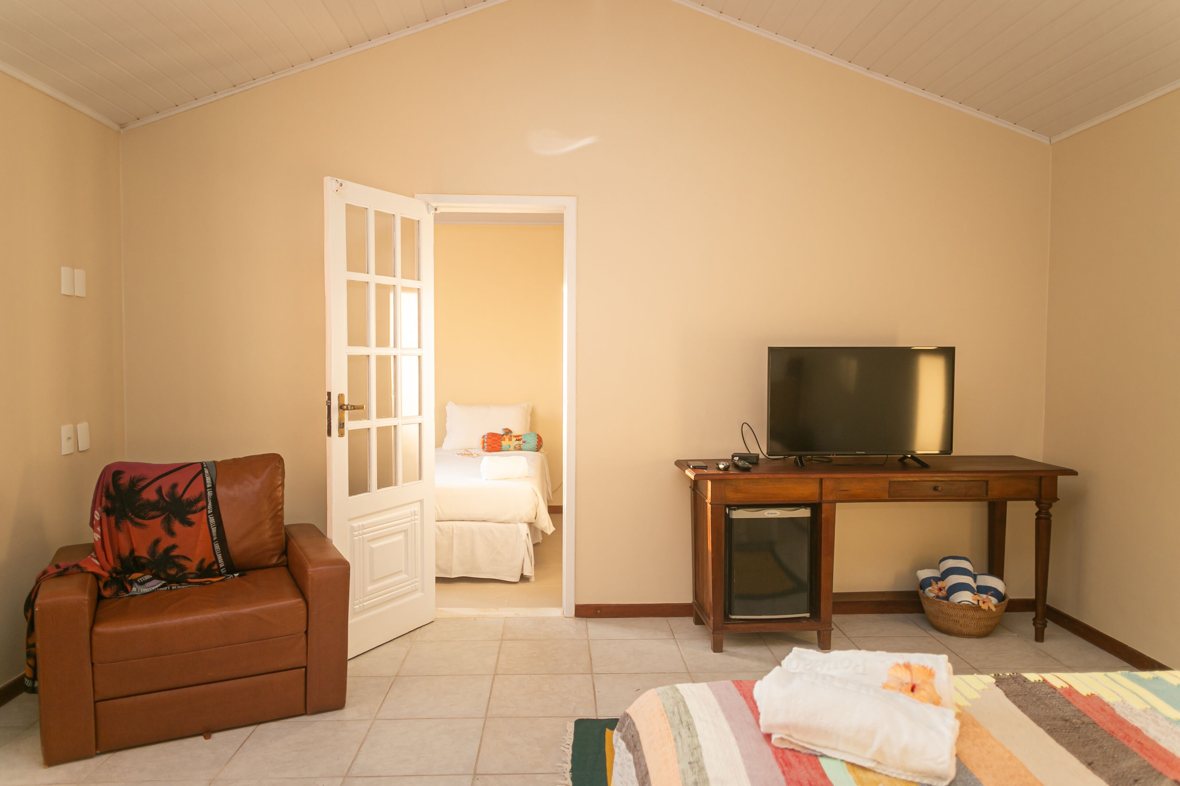 Ein Hotelzimmer mit einem Bett, einem Fernseher, einem kleinen Tisch, einem Sofa und einer Tür zu einem anderen Raum.