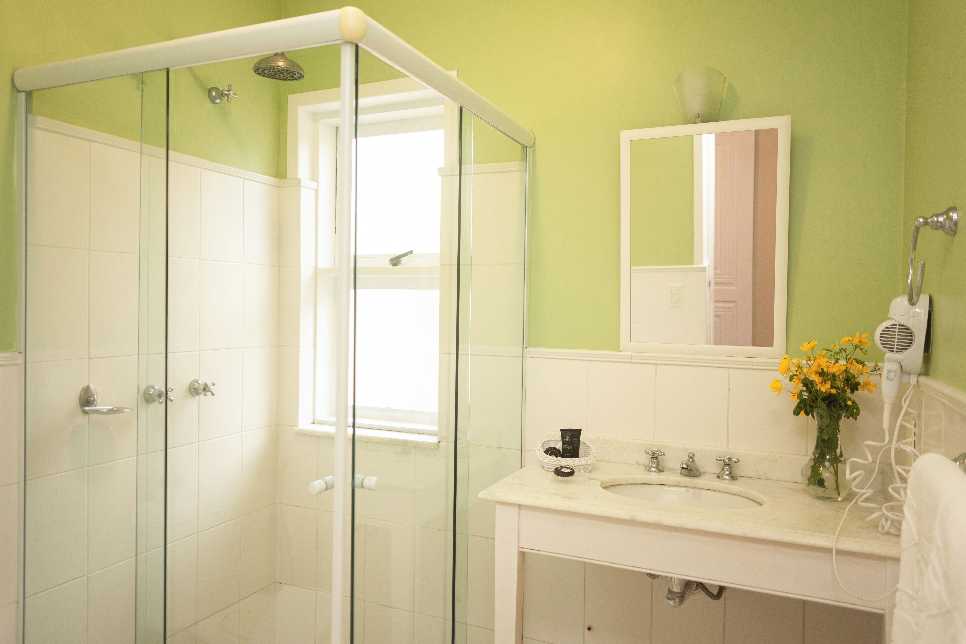 A bathroom with a glass-enclosed shower, a sink with a mirror above it, and a vase with flowers on the counter.