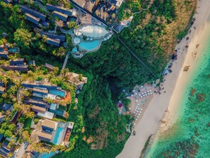 An aerial view of a resort with multiple buildings, a large swimming pool, and a beach area with umbrellas. - Karma Kandara (Ungasan)