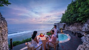 A dinner table with four people, a pool, and a view of the ocean.