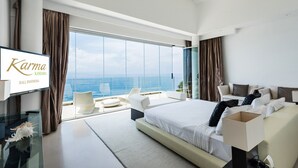 A modern hotel room with a large bed, a glass table, and a view of the ocean.