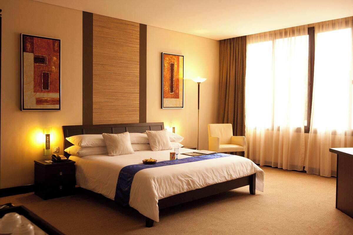 Una habitación de hotel con una cama grande, una mesita de noche con lámpara, una silla y cuadros en las paredes.