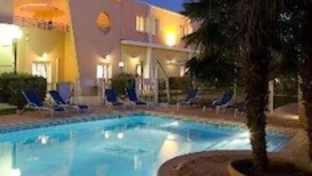 Un hôtel doté d’une piscine, de chaises longues et d’un palmier.