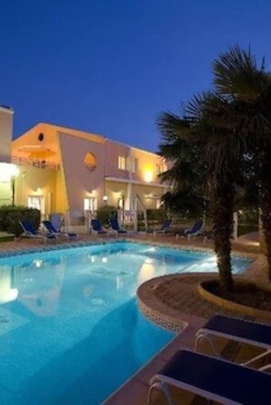 A hotel with a swimming pool, lounge chairs, and a palm tree. - Hôtel Ariane (Istres)