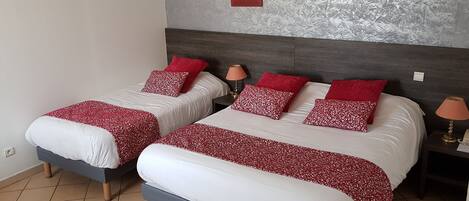 A hotel room with two beds, each with white and red patterned bedding, a grey headboard, a wall-mounted lamp, and a framed picture.