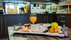 Un plateau de petit-déjeuner avec des croissants, une tasse de café, un verre de jus d’orange et un bol de fruits, le tout posé sur une table recouverte d’une nappe à rayures.