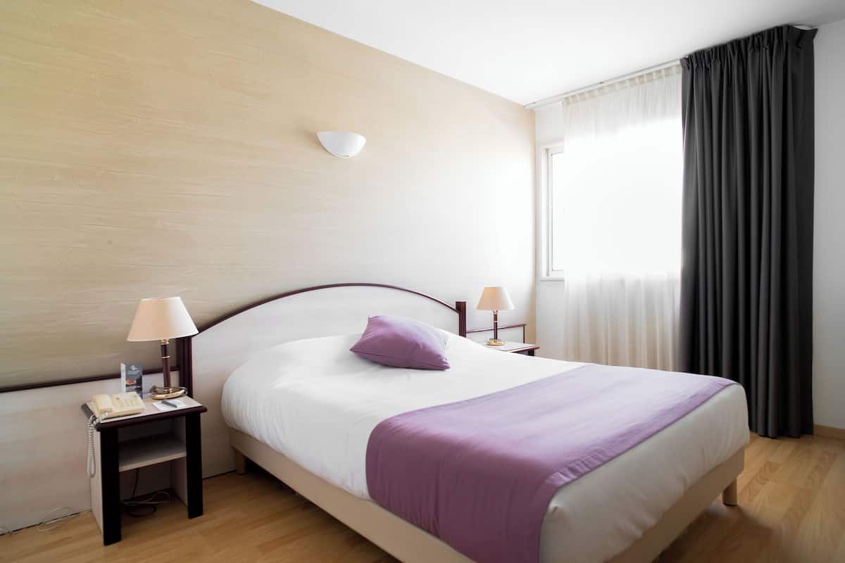 A neatly made bed with a purple pillow, a bedside lamp, and a telephone on a wooden nightstand.