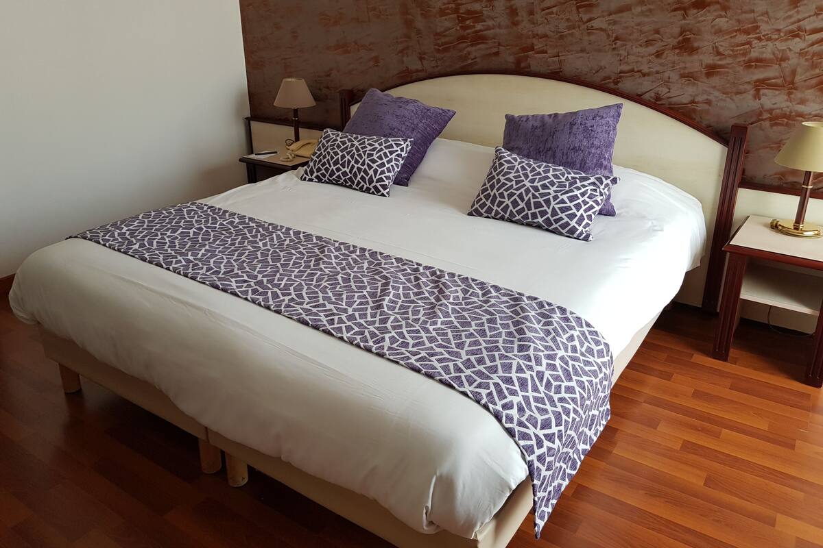 A neatly made bed with a patterned bedspread and pillows, a bedside lamp, and a nightstand with a telephone.