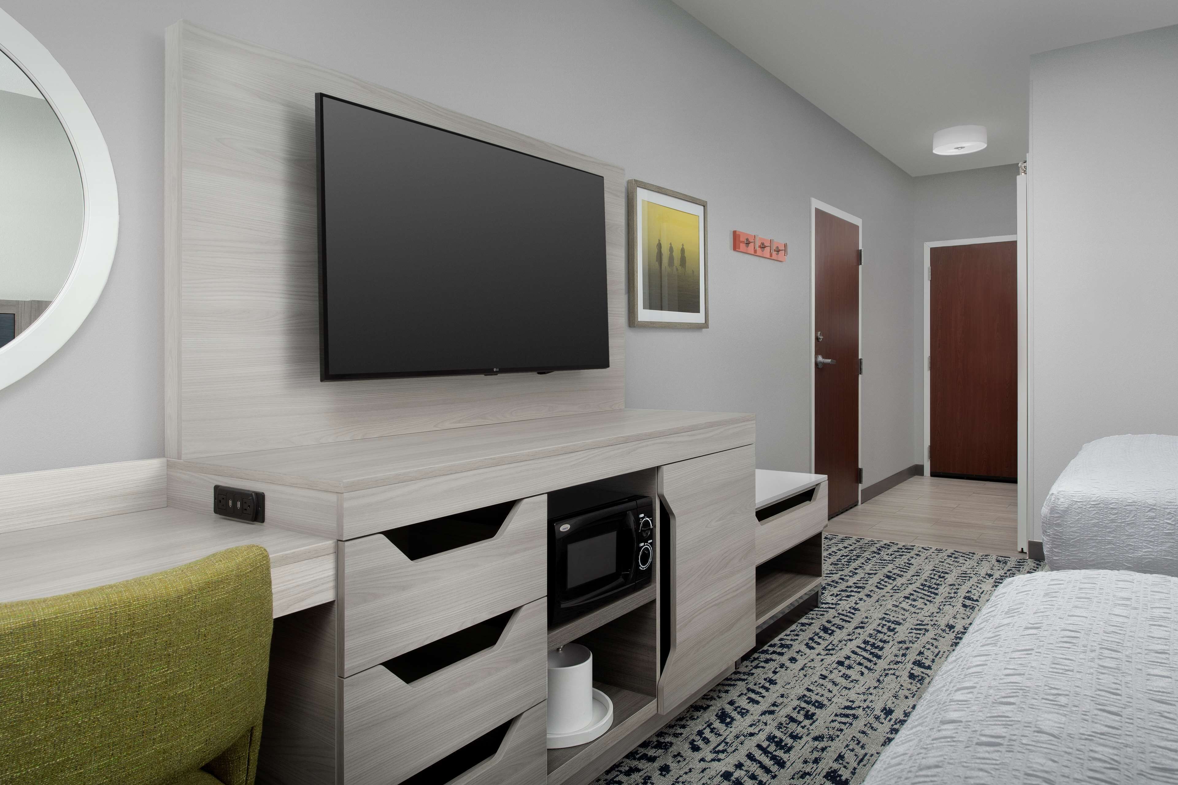 Una habitación de hotel moderna con televisión de pantalla plana, microondas, un armario de madera, cama y puerta.