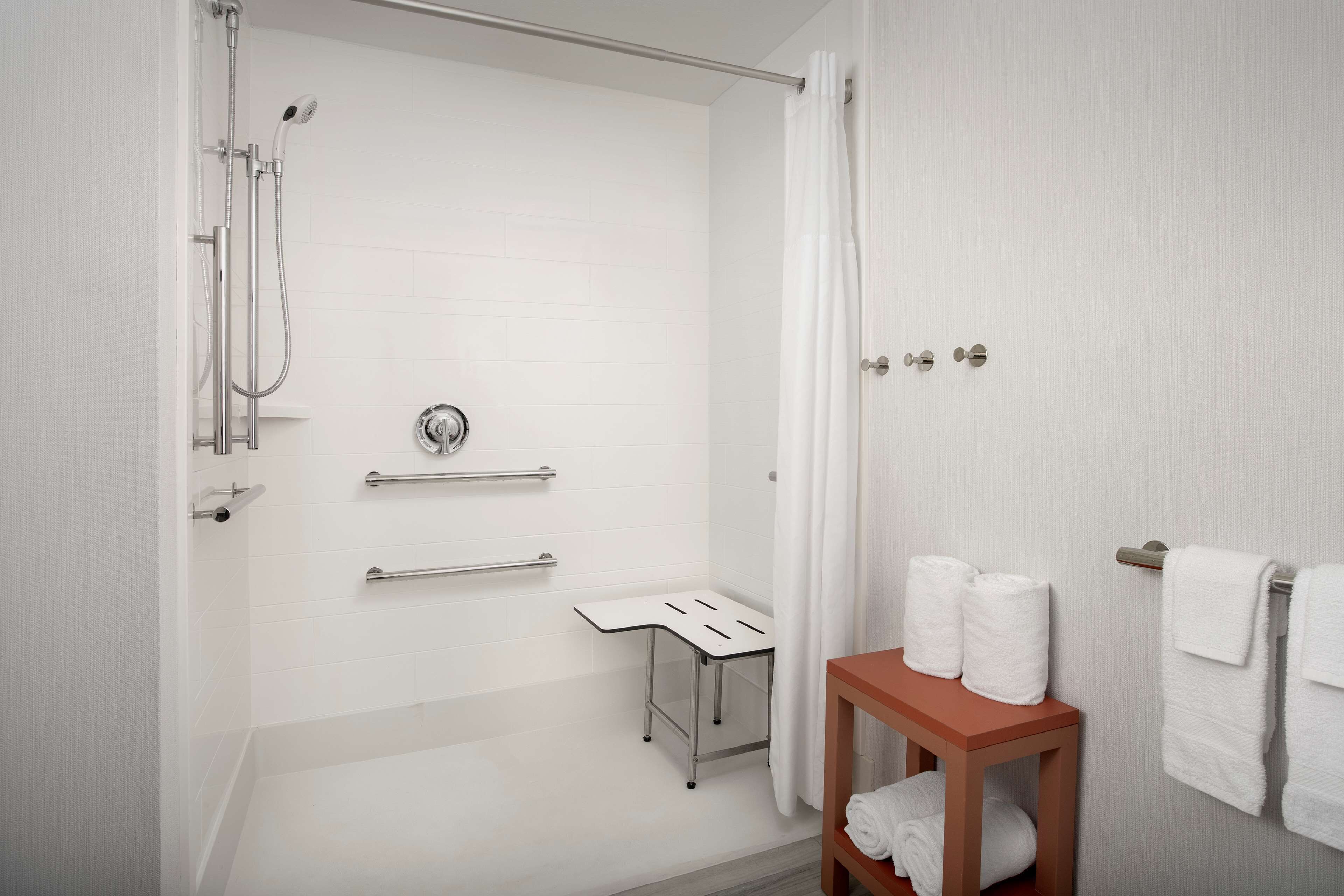 Une salle de bain moderne équipée d’une douche, de barres d’appui, d’un porte-serviettes et d’une table en bois sur laquelle sont posées des serviettes.