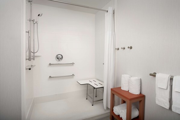 A modern bathroom with a shower, grab bars, a towel rack, and a wooden table with towels.