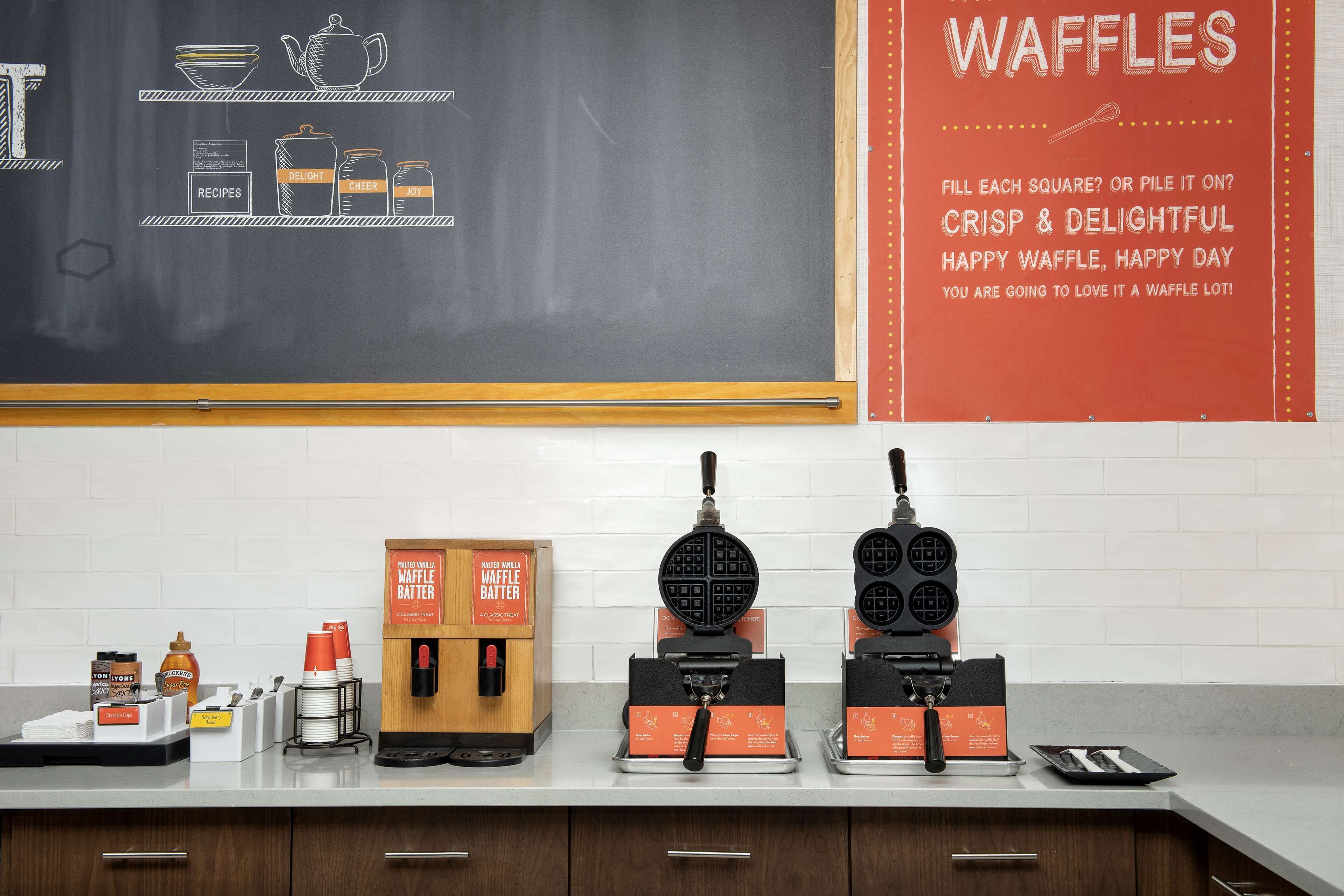A kitchen counter with waffle makers and waffle batter boxes.