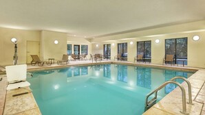 Une piscine intérieure à l’eau claire, entourée de chaises longues et de tables, et dotée de grandes fenêtres qui laissent entrer la lumière naturelle.