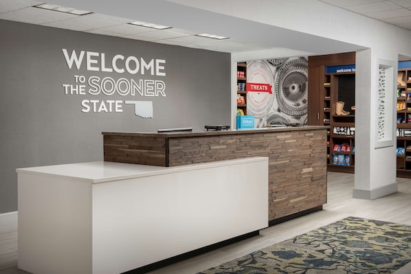 En receptionsdisk med en skylt som säger ”Välkommen till delstaten Sooner”, en skylt som säger ”Godbitar” och en skylt med texten ”Hilton”.
