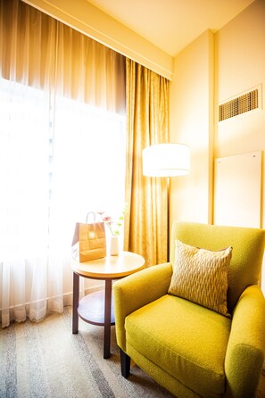 A room with a yellow armchair, a small round table, a lamp, and a window with curtains.