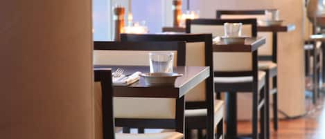 Un interior de restaurante con mesas y sillas de madera, lámparas colgantes y un suelo de madera pulida.