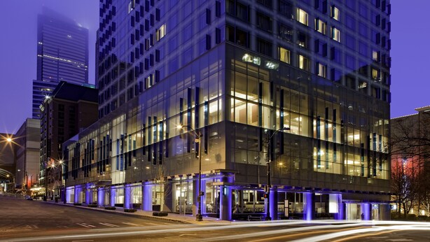 Un hotel moderno con fachada de vidrio, varios pisos y ventanas iluminadas.