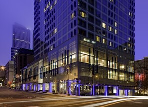A modern hotel with a glass facade, multiple floors, and illuminated windows.