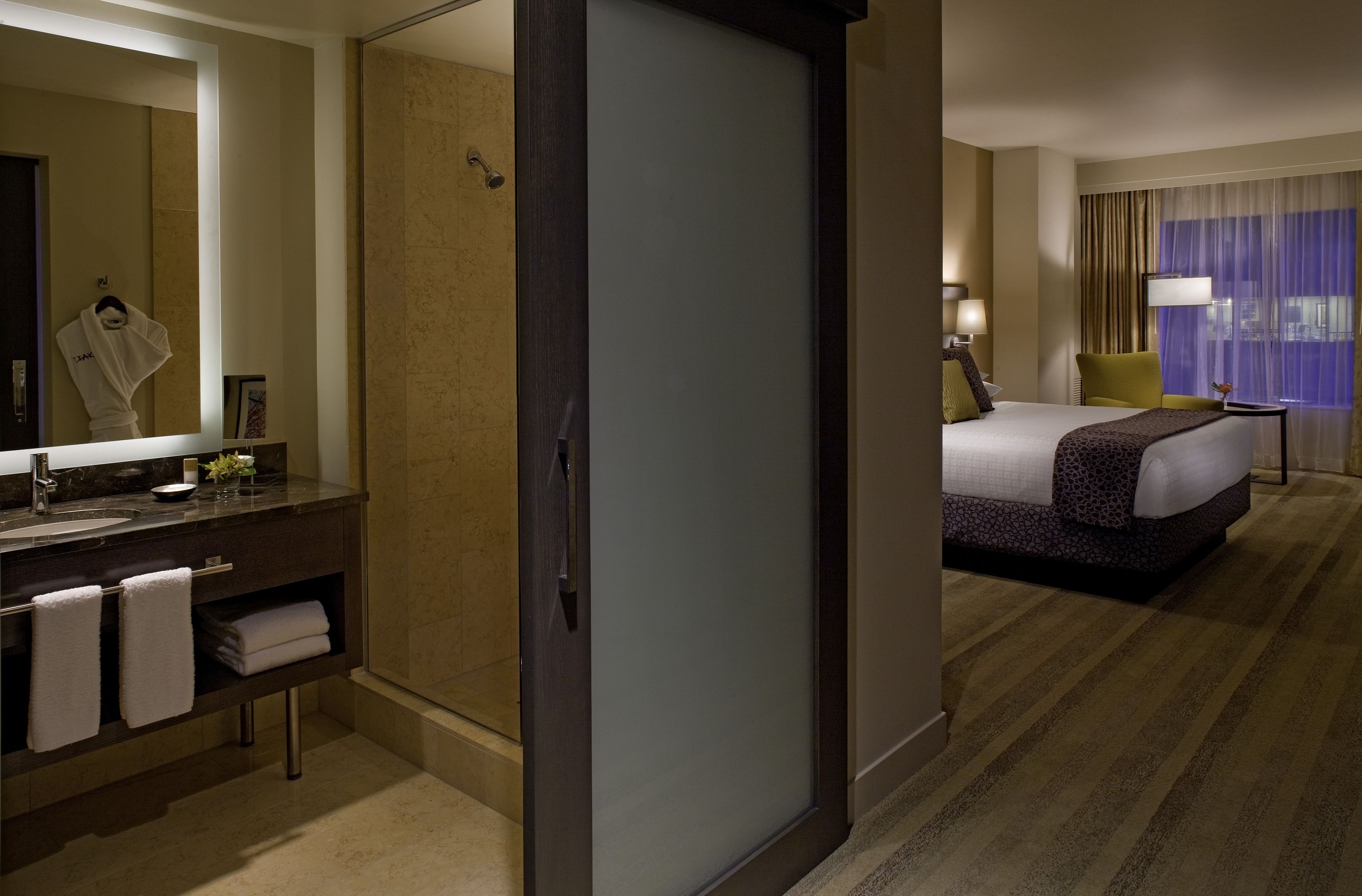 Habitación de hotel con una cama grande, baño con espejo y vistas de la ciudad por la ventana.
