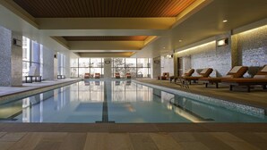 Una amplia piscina interior con sillones de descanso y vistas a un edificio a través de grandes ventanales.