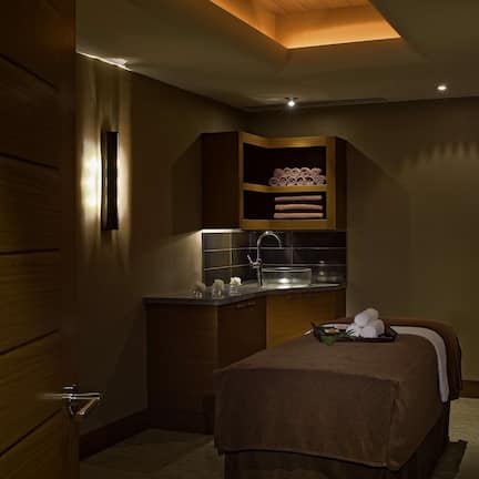 A compact hotel room with a bed, a small kitchenette, and a built-in shelf with towels.