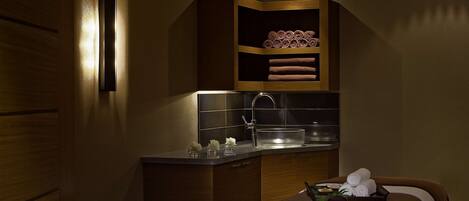 Una habitación de hotel compacta con cama, una kitchenette pequeña y un estante empotrado con toallas.