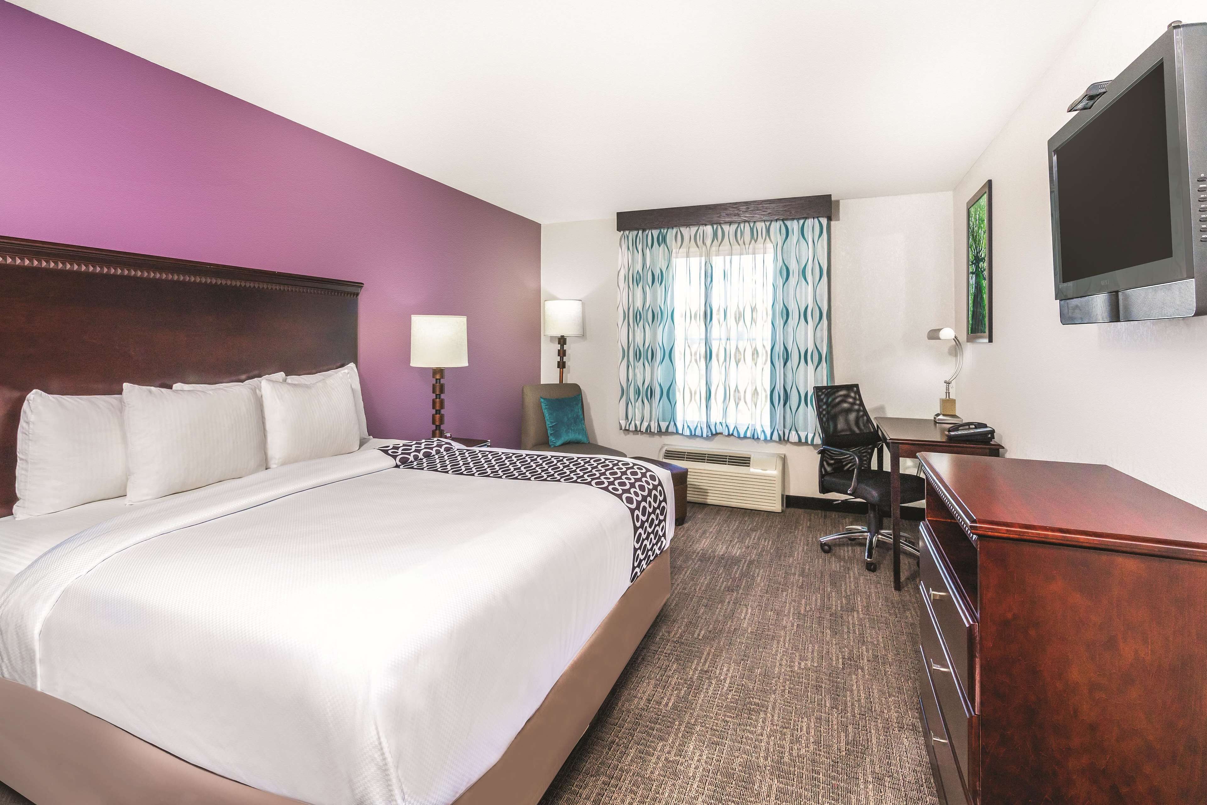 A hotel room with a large bed, a desk, a chair, a TV, and a window with curtains.