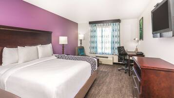 A hotel room with a large bed, a desk, a chair, a TV, and a window with curtains.