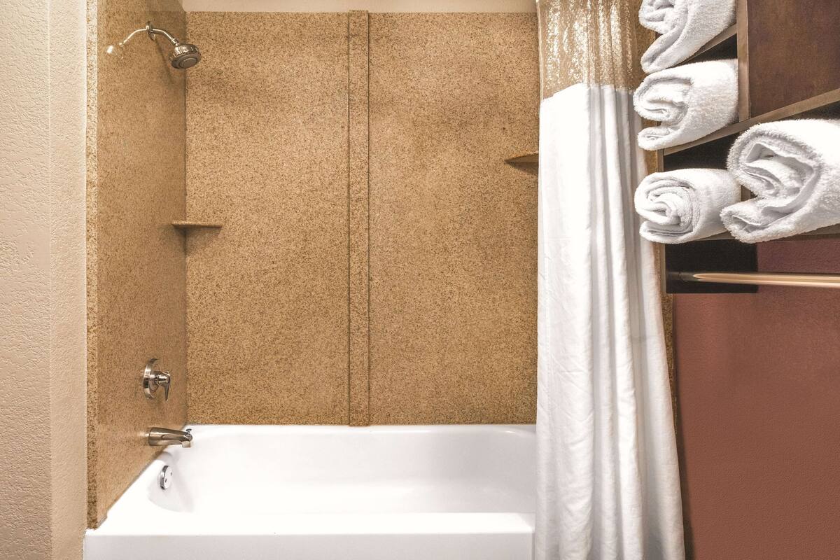 Un baño con bañera, ducha y un perchero con toallas ordenadamente dobladas.