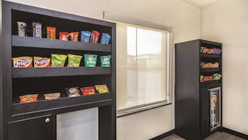 Habitación de hotel con estantes para aperitivos y un refrigerador pequeño.