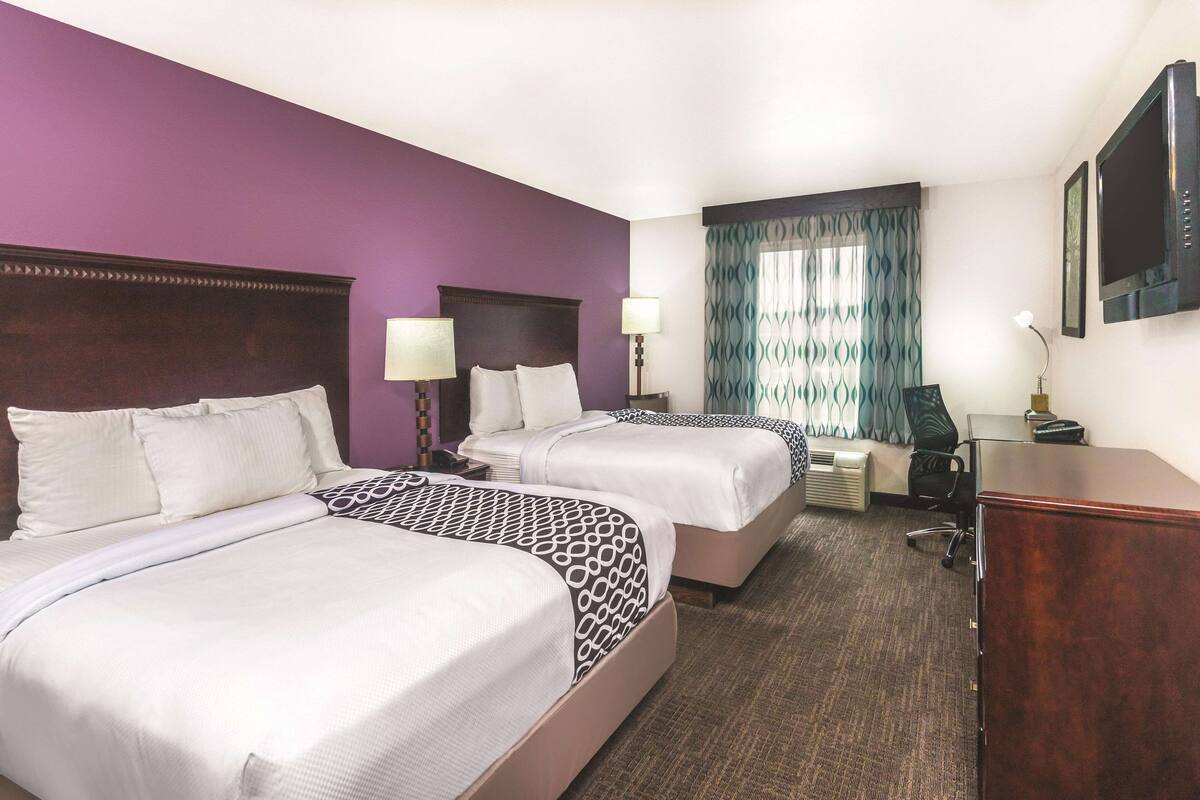 Habitación de hotel con dos camas, un escritorio, una silla y un televisor.