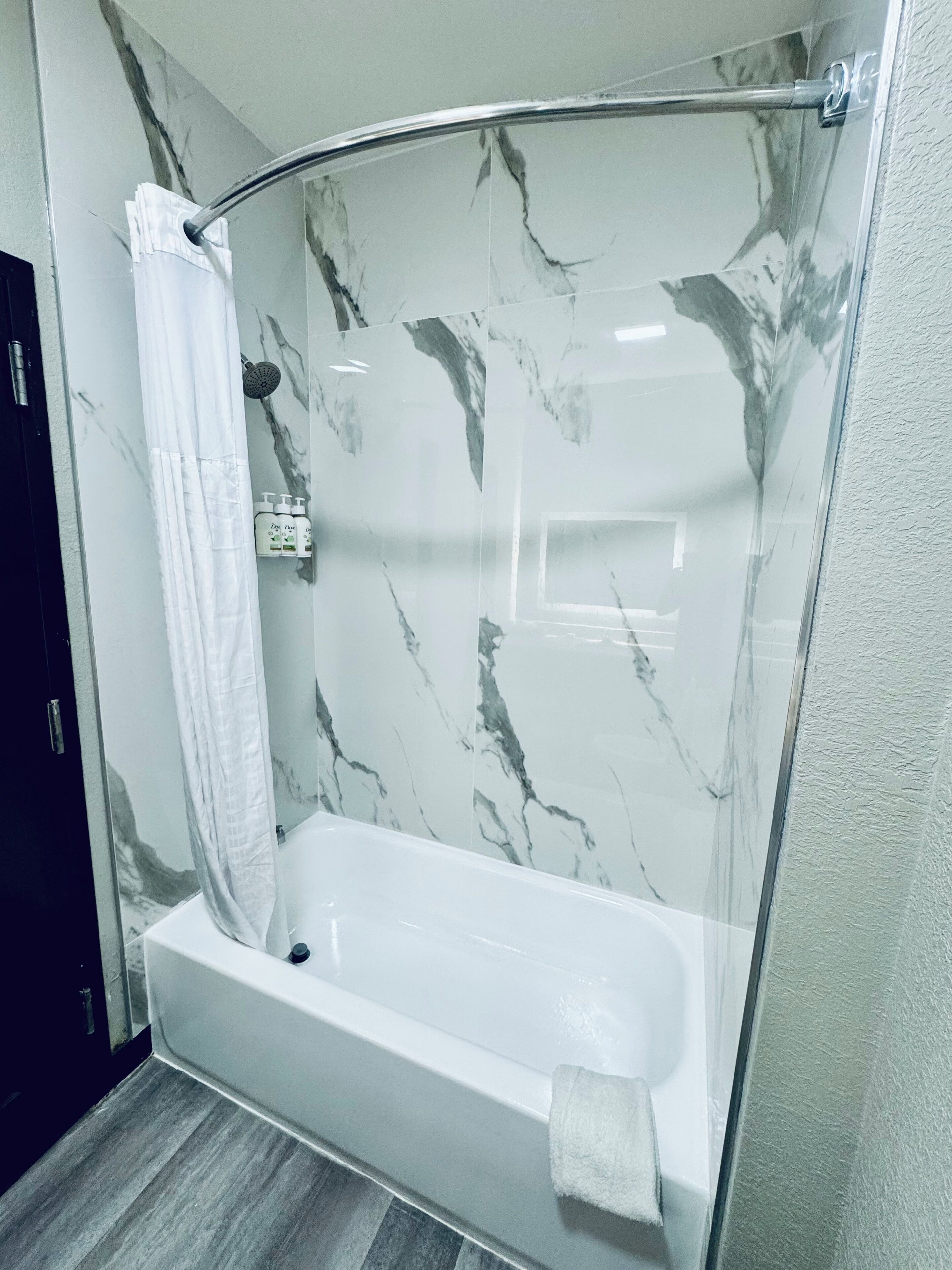 A modern bathroom with a glass-enclosed shower, a white bathtub, and marble-patterned walls.