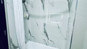 A modern bathroom with a glass-enclosed shower, a white bathtub, and marble-patterned walls.
