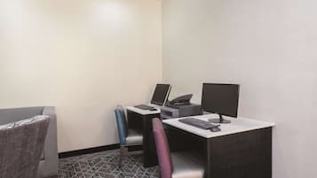 A hotel room with a desk, two chairs, a laptop, a desktop computer, and a printer.