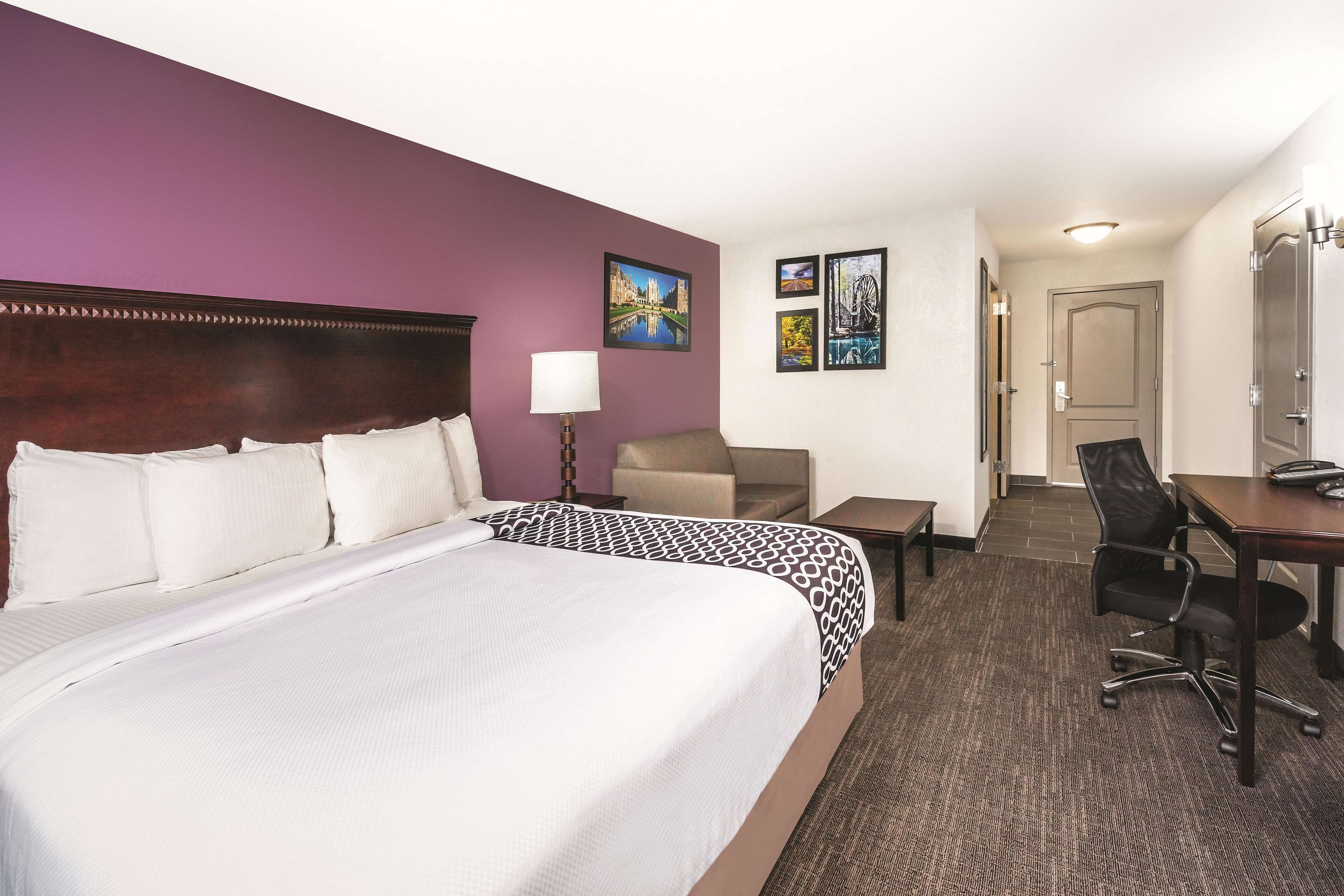 A hotel room with a large bed, a desk, a chair, and a lamp.