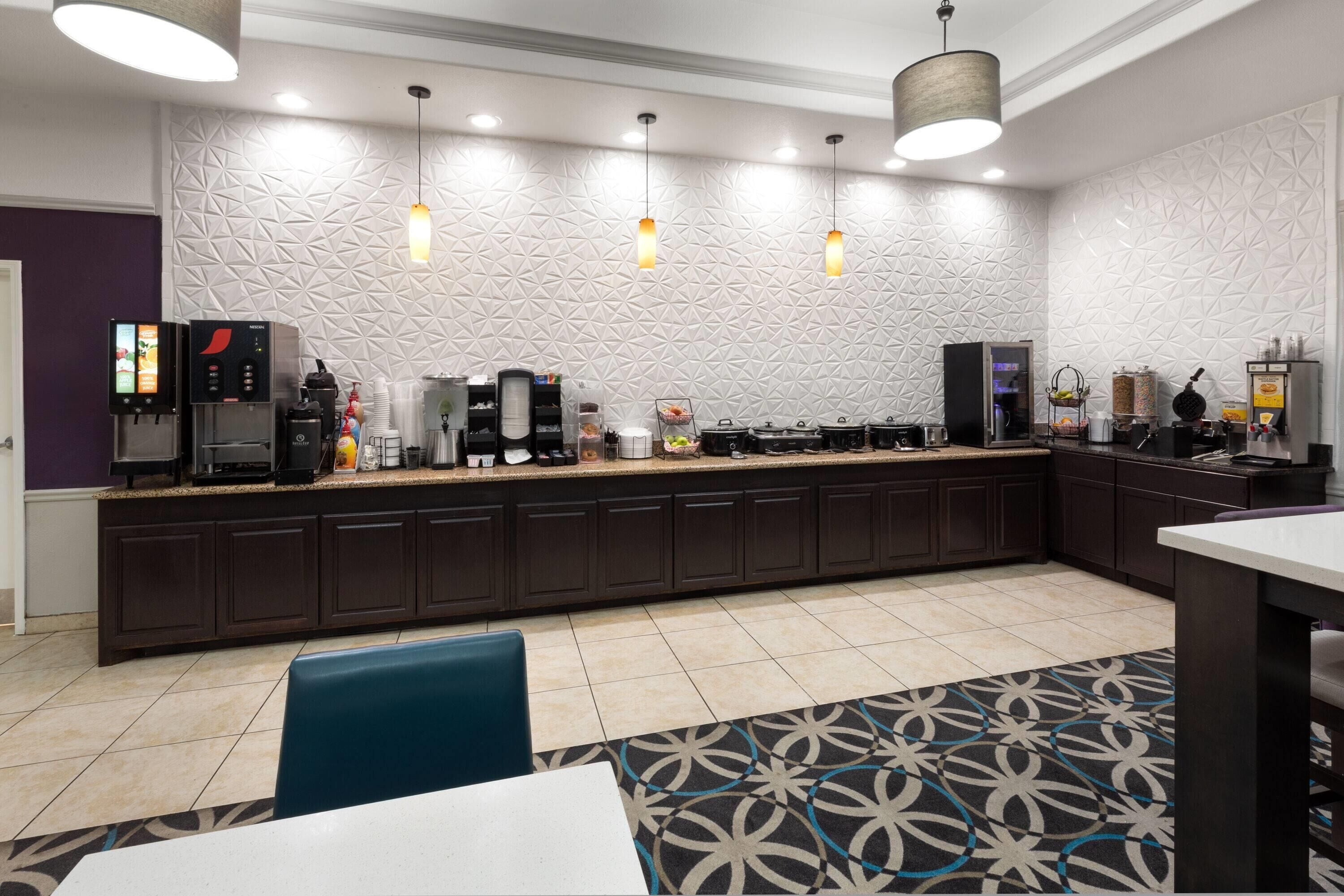En modern hotellobby med en lång receptionsdisk, kaffemaskiner och en mönstrad matta.