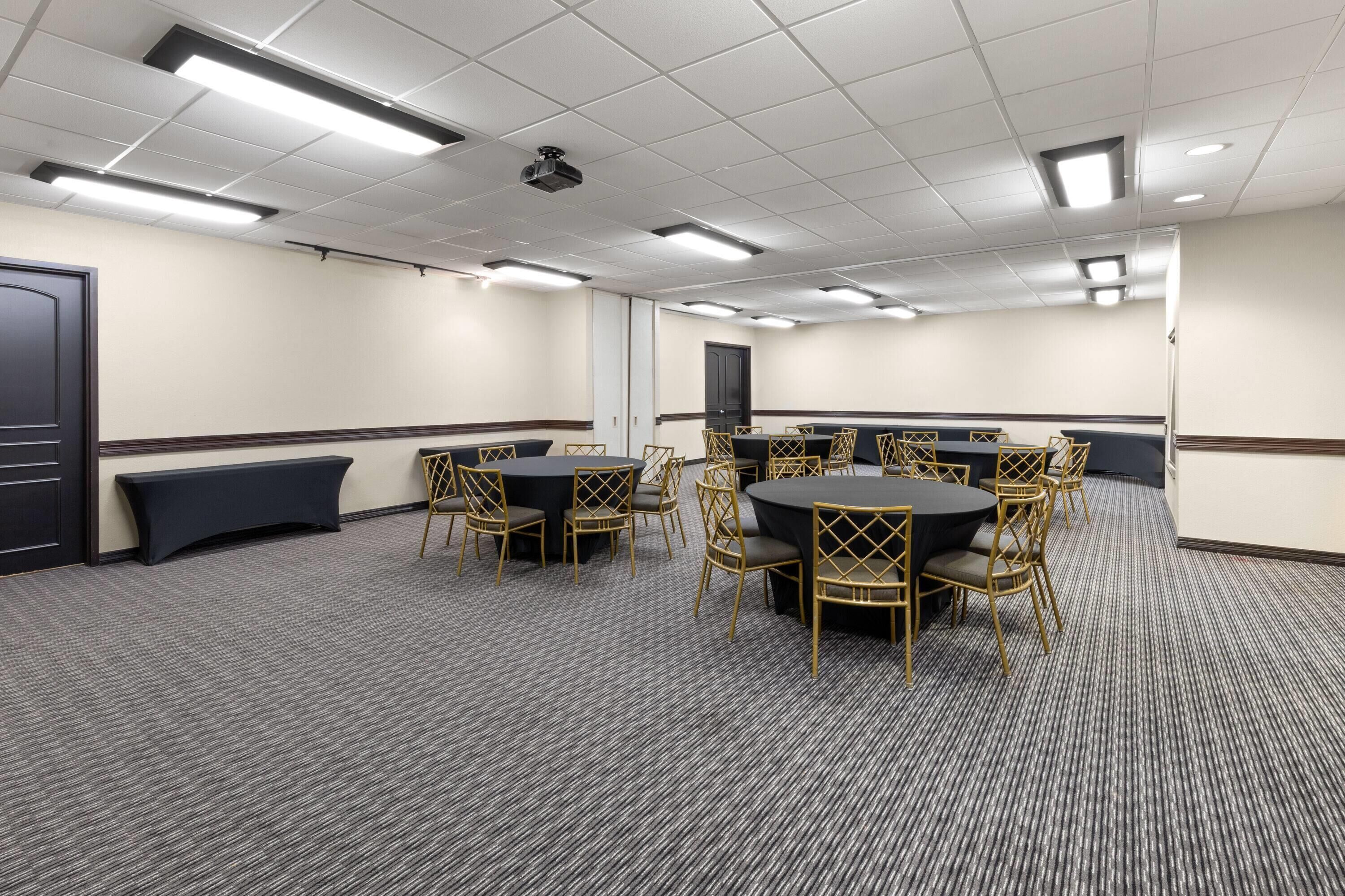 A conference room with round tables, chairs, and a carpeted floor.