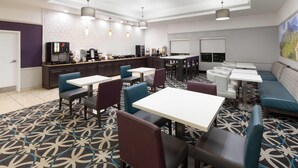 Un moderno vestíbulo de hotel con varias zonas de estar, incluyendo mesas y cabinas, y una estación de café.
