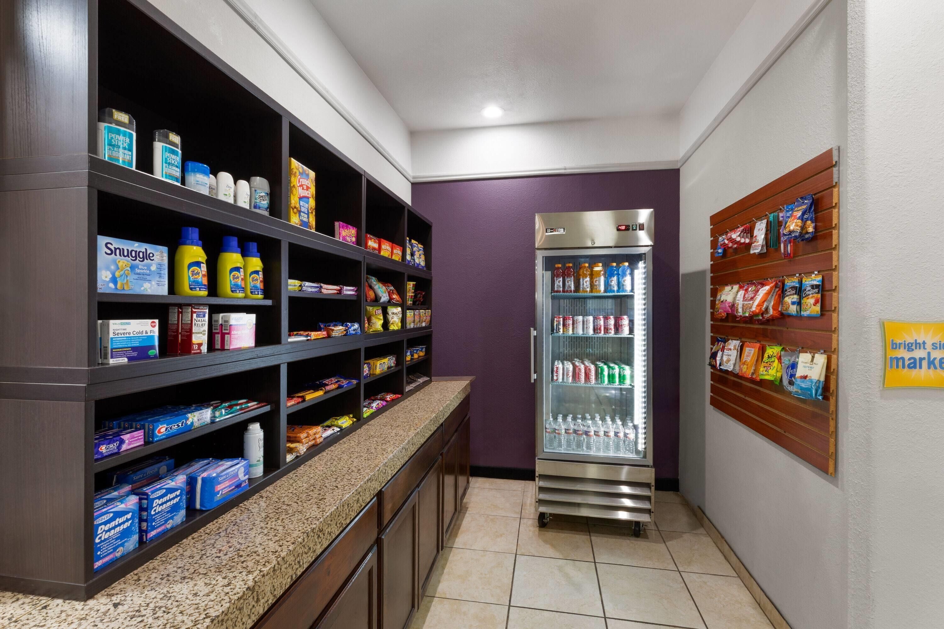 A self-service beverage station with a refrigerated drink dispenser and shelves stocked with various beverages and snacks.