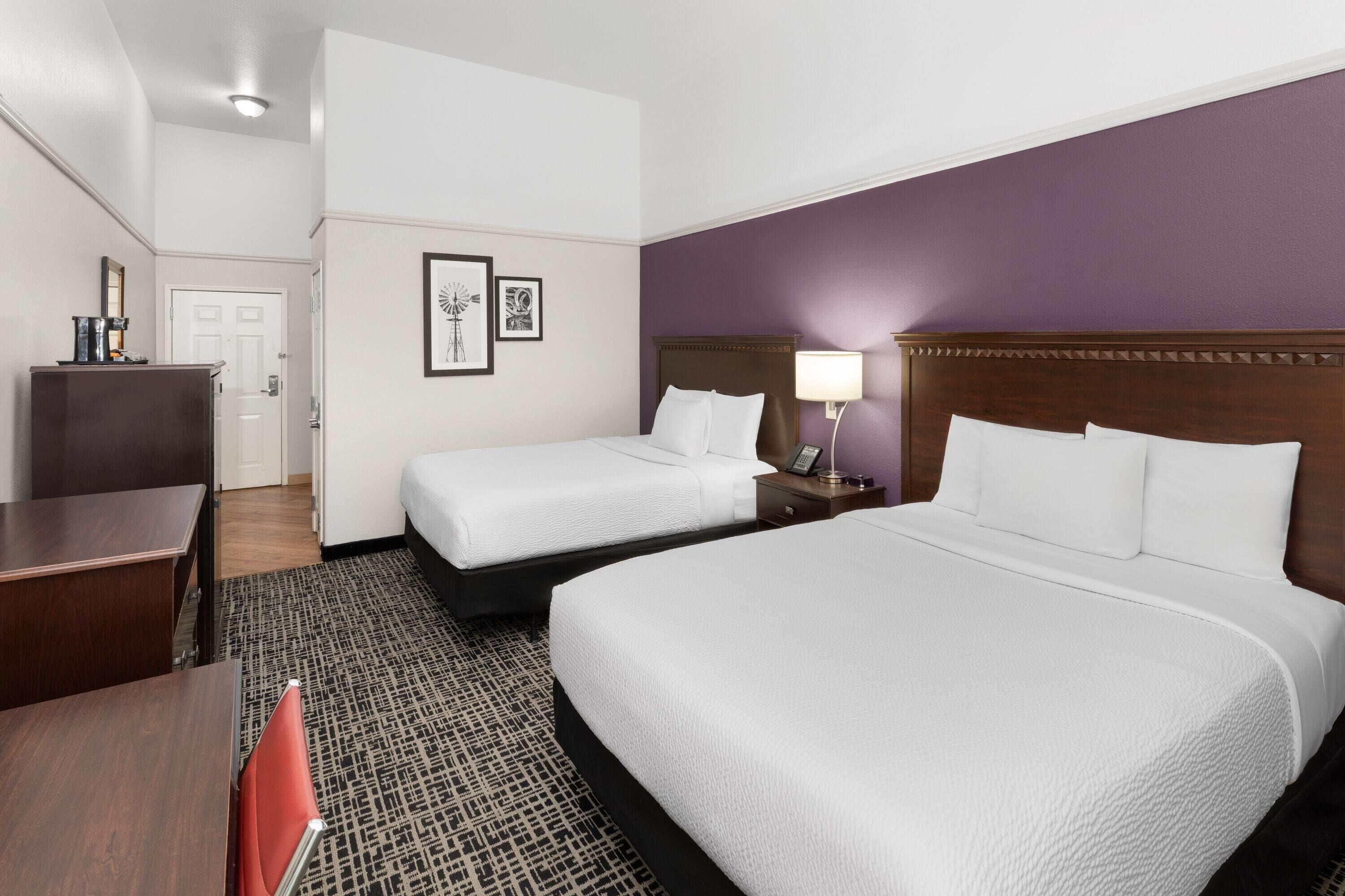 A hotel room with two single beds, a desk, a chair, and a small table.