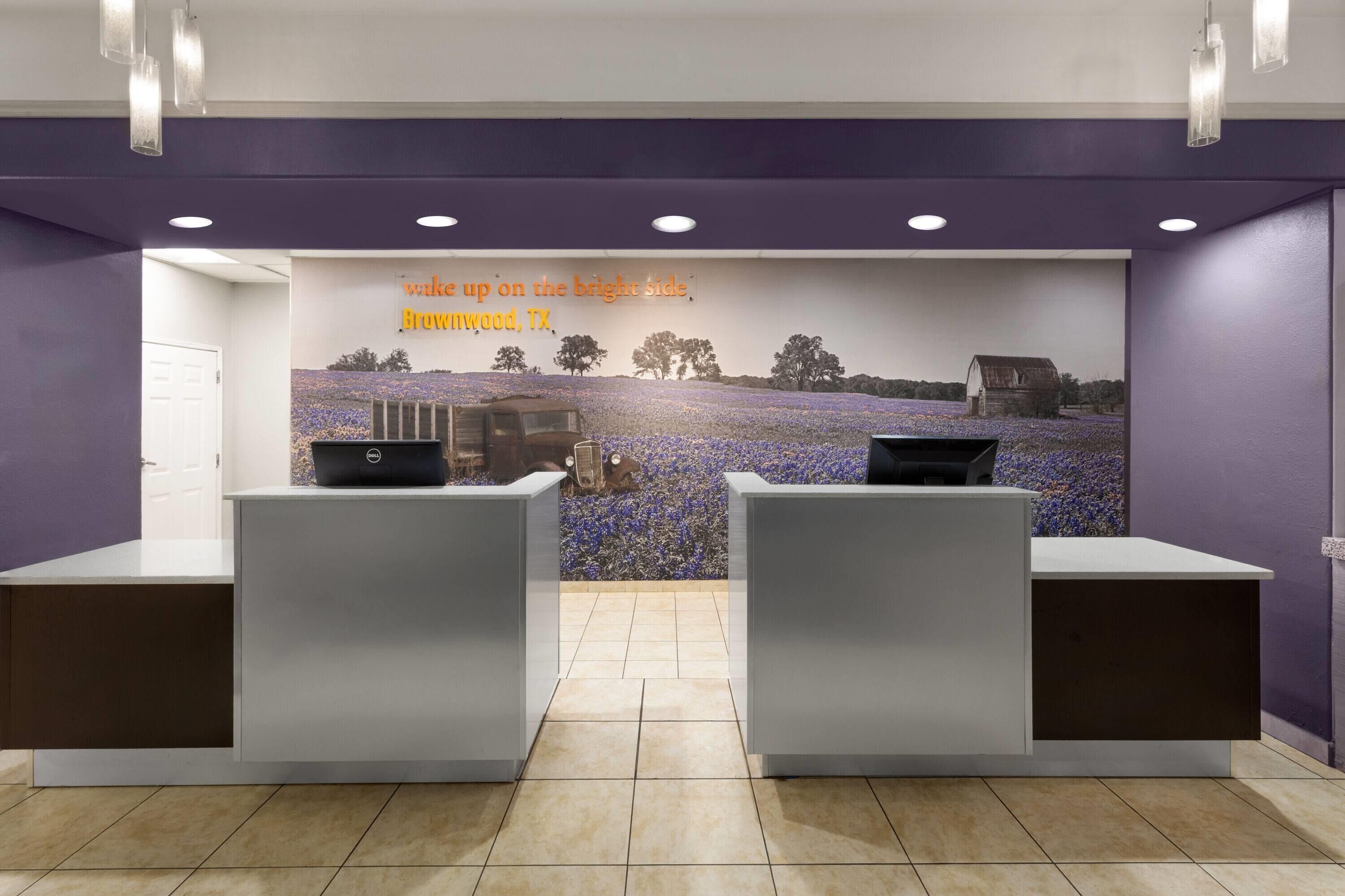 Zona d'arribada amb dues taules de recepció, una paret morada i un mural d'un camp amb una granja.