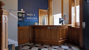 A reception area with a blue wall, wooden reception desk, and a check-in counter. - Travelodge Edinburgh Haymarket (Edinburgh)