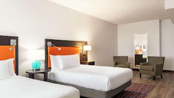 Habitación de hotel con dos camas, una mesa redonda con lámpara, una silla y un espejo.