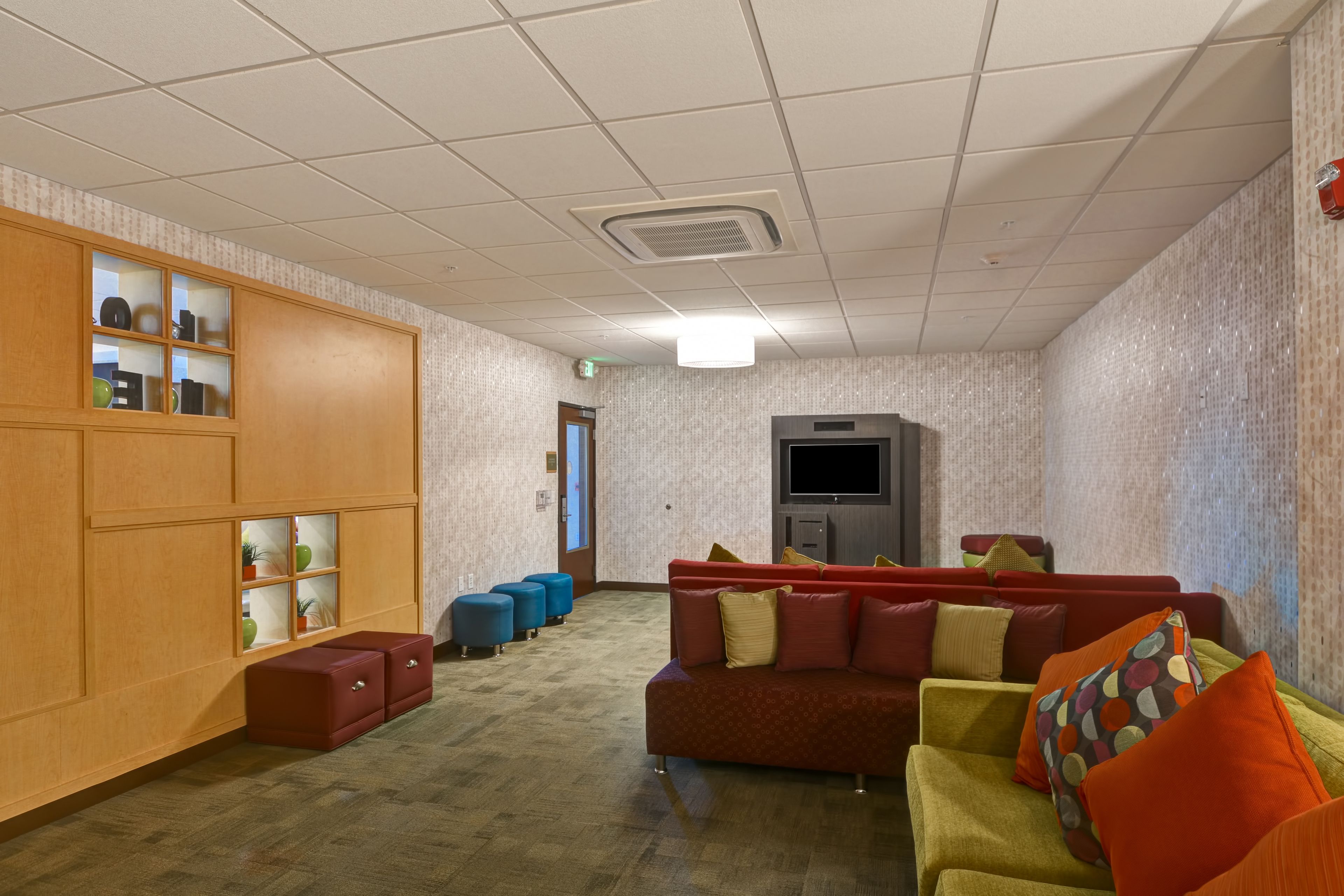 A spacious lobby with a wooden panel wall, a red sofa, and blue ottomans.