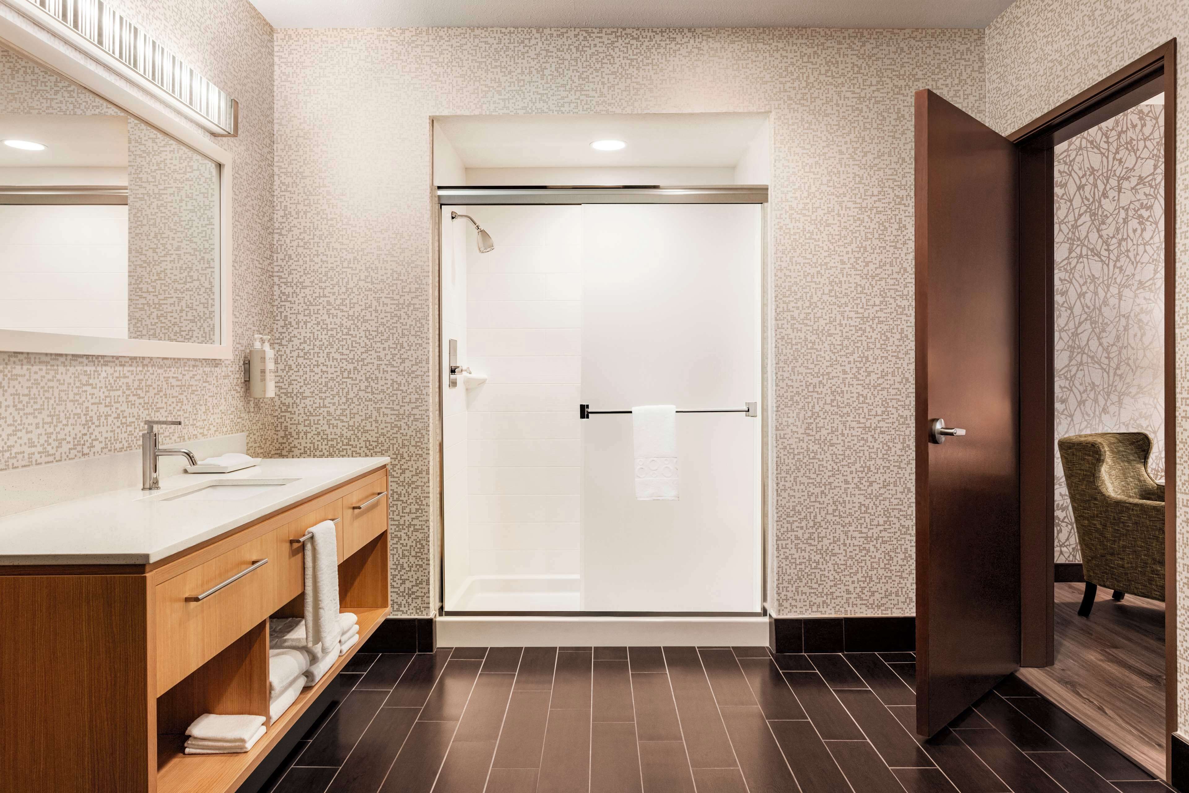 A modern bathroom with a shower, a vanity with a mirror, and a chair.