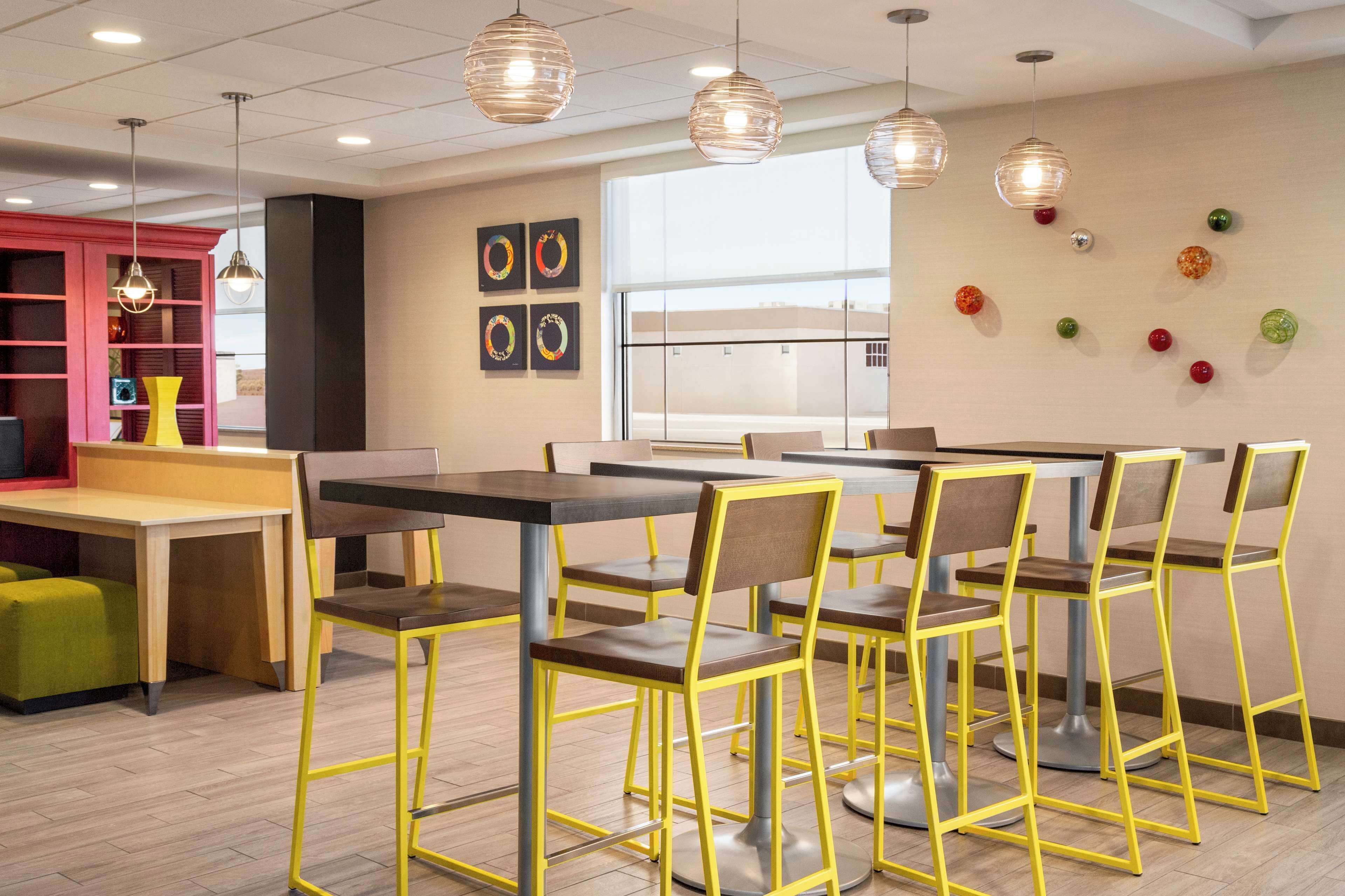 A modern cafeteria with yellow chairs and tables, a red bookshelf, and decorative wall art.