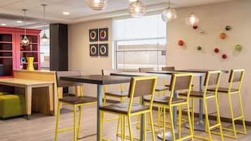 A modern cafeteria with yellow chairs and tables, a red bookshelf, and decorative wall art.