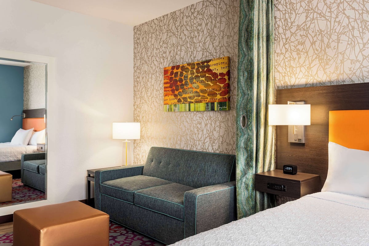 Ett hotellrum med en säng, en soffa, ett litet bord och en spegel.