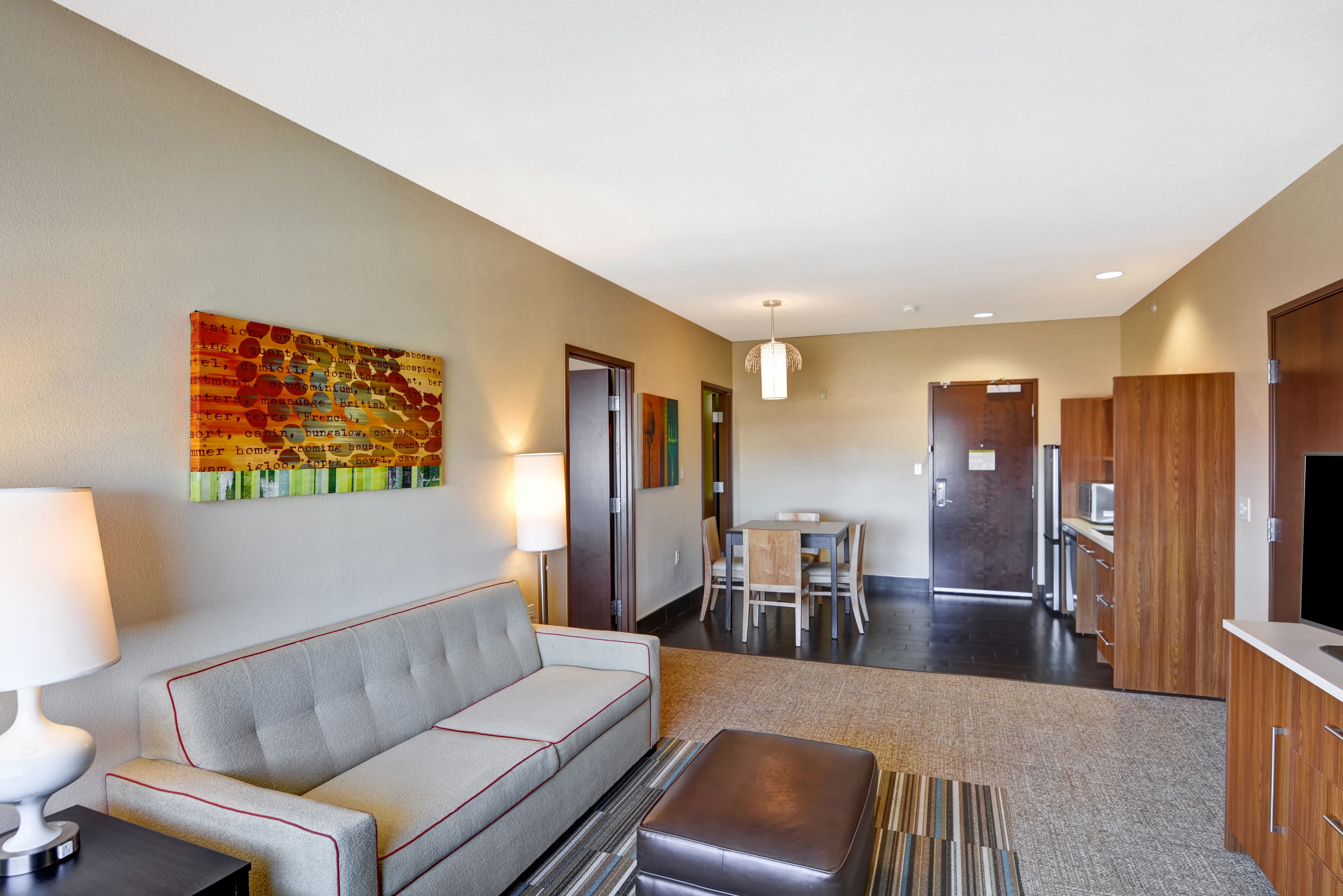 Habitación de hotel con sofá, lámpara, pintura, mesa de comedor y zona de cocina.